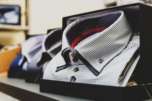 Close-up of neatly folded, checkered dress shirts in display boxes. The shirts feature a black and white pattern with contrasting buttons, stacked on a store shelf.